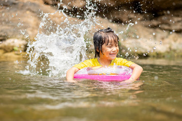 Obraz premium Asian girl in pool ring playing water in stream, Little female kid with pool ring kicking water splash, Water activity