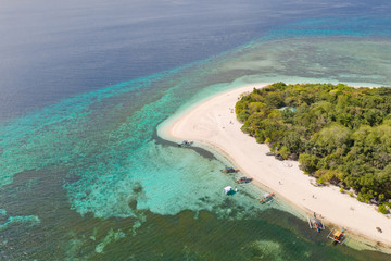 Fototapeta na wymiar A small island surrounded by azure water and coral reefs, a top view.Round tropical island with white sandy beach, top view.Mantigue Island, Philippines.