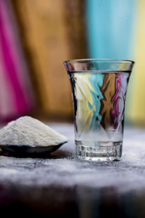 Rice water in a glass bowl along with rice grains & its powder also on wooden surface & some rice power spread on the surface for the treatment of various things such as Home Remedy,Beauty & Health.
