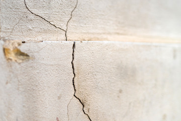 Old foundation and plaster wall with cracks. Building requiring repair closeup.