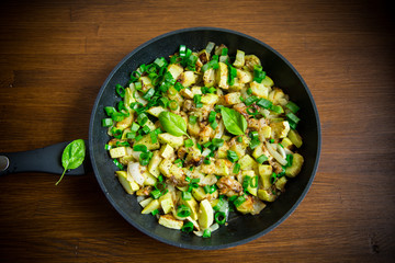 zucchini fried with onions and herbs in a pan on a wooden table