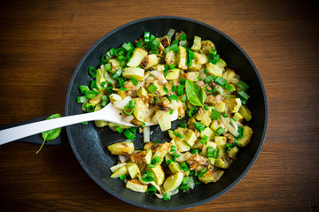 zucchini fried with onions and herbs in a pan on a wooden table