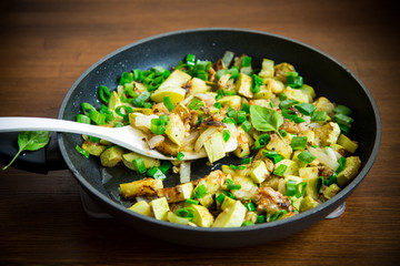 zucchini fried with onions and herbs in a pan on a wooden table