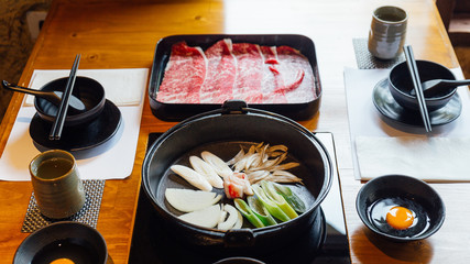 Sukiyaki set: Premium Rare Slices Wagyu beef with high-marbled texture on black rectangle plate, vegetables in hot pot and raw egg.