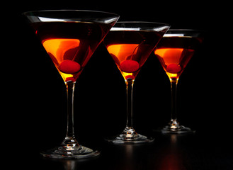 Group of three manhattan cocktails in bar on black
