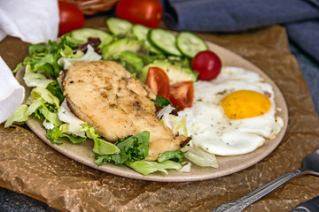Served healthy breakfast with fried eggs and vegetable Top view of plate of tasty fried eggs with chicken and avocado with colorful vegetable salad placed next to knife and fork on kitchen table
