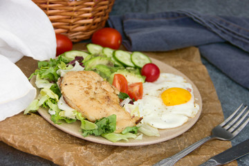 Served healthy breakfast with fried eggs and vegetable Top view of plate of tasty fried eggs with chicken and avocado with colorful vegetable salad placed next to knife and fork on kitchen table