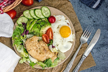 Served healthy breakfast with fried eggs and vegetable Top view of plate of tasty fried eggs with chicken and avocado with colorful vegetable salad placed next to knife and fork on kitchen table