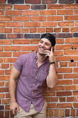 Handsome Young Man on Cellphone Texting and Call Conversation with Backwards Hat Smiling for Portraits in Front of Textured Brick Wall Outside