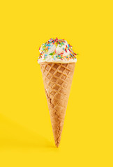 white ice cream ball in a Waffle Cone on a yellow Background. Fruit ice cream in a waffle cone.