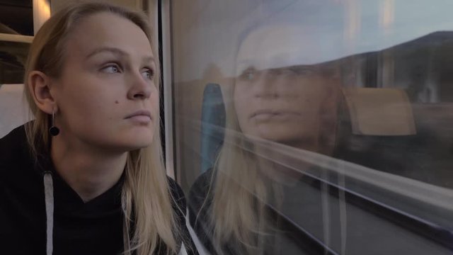 Young blond woman enjoying landscapes in the window of moving train. Railway journey