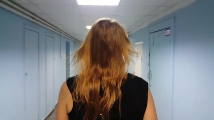 Back steadicam shot of a blond woman walking through the long hospital hallway with empty seats