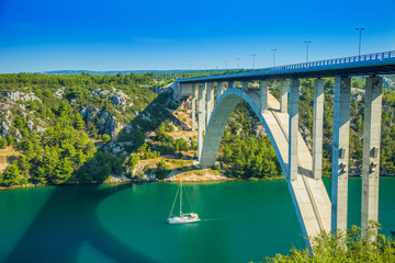 Aerial panorama view of bridge on highway over Krka river in deep canyon in Croatia and sailing boat passing under. Beautiful landscape.