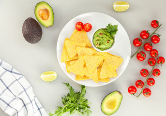 A delicious Bowl of Guacamole next to fresh ingredients on a table with tortilla chips. Traditional latin american mexican sauce guacamole on grey background. Top view.