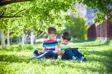 Two brother kid is lying on the grass with tablet.