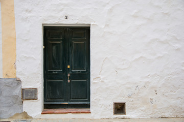 Old green wooden door surrounded by a plain white wall.