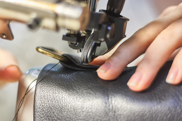 Sewing machine in a leather workshop in action with hands working with a leather details