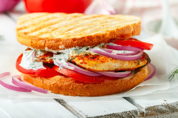 Sandwich with fried chicken breast, tomatoes, red onions and tzatziki sauce. Gourmet appetizer. Selective focus