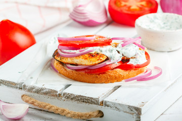 Sandwich with fried chicken breast, tomatoes, red onions and tzatziki sauce. Gourmet appetizer. Selective focus