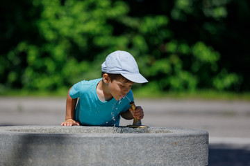 the boy is drinking water from the fountain. kid drinks water. Outdoor shot of a child drinking water from a tap or water or fountain.