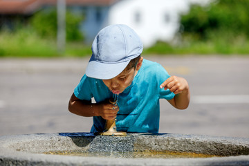 the boy is drinking water from the fountain. kid drinks water. Outdoor shot of a child drinking water from a tap or water or fountain.