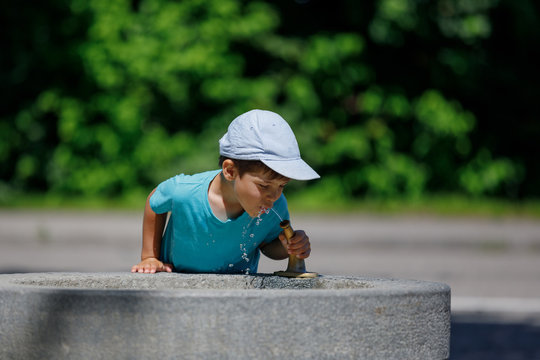 The Boy Is Drinking Water From The Fountain. Kid Drinks Water. Outdoor Shot Of A Child Drinking Water From A Tap Or Water Or Fountain.