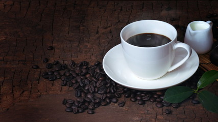 A cup of hot coffee and fresh coffee beans on an old brown wood background