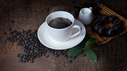 A cup of hot coffee and fresh coffee beans on an old brown wood background