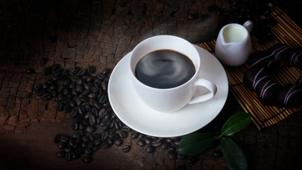 A cup of hot coffee and fresh coffee beans on an old brown wood background