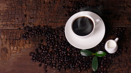 A cup of hot coffee and fresh coffee beans on an old brown wood background