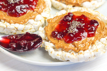 crunchy natural peanut butter strawberry jam jelly sandwich with chia seeds on rice cake bread. Proper nutrition diet vegetarian breakfast on plate next to knife with peanut butter