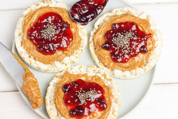 crunchy natural peanut butter strawberry jam jelly sandwich with chia seeds on rice cake bread. Proper nutrition diet vegetarian breakfast on plate next to knife with peanut butter