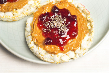 crunchy natural peanut butter strawberry jam jelly sandwich with chia seeds on rice cake bread. Proper nutrition diet vegetarian breakfast on plate next to knife with peanut butter