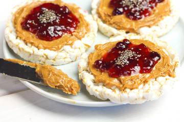 crunchy natural peanut butter strawberry jam jelly sandwich with chia seeds on rice cake bread. Proper nutrition diet vegetarian breakfast on plate next to knife with peanut butter