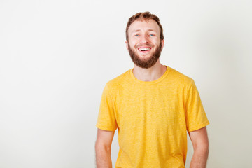 Portrait of young beard man in yellow shirt with blue eyes smiling laughing looking at camera over gray background.