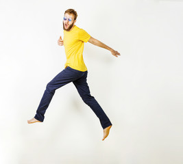 Fototapeta na wymiar Full-length photo of beard man in casual yellow t-shirt and jeans running or jumping in air makes funny faces over gray background