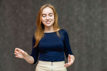 Portrait of a knee-high beautiful pretty red-haired woman girl in a blue jacket with a light skirt on a gray background in the studio. Smiles, shows emotions, talks, spreads his hands.