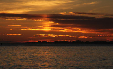 Dark ocean Sunset in dark orange and sun relection on clouds