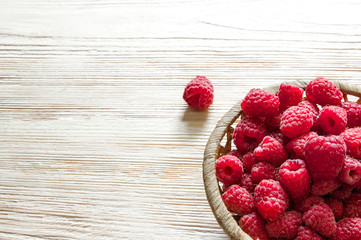 raspberries in a basket on a light wooden background
