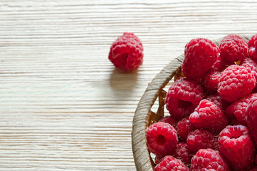 raspberries in a basket on a light wooden background