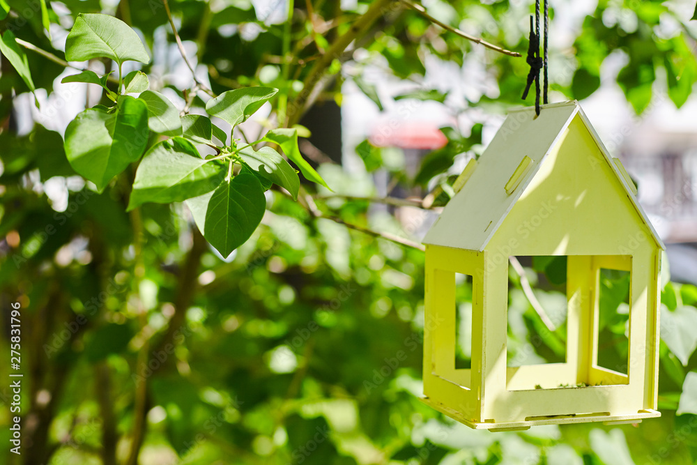 Wall mural yellow bird house hanging from the tree and surrounded by lush foliage. nest box on a green backgrou