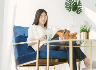 Portrait Asian woman reading book and relaxing with coffee at home