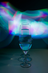 A three wine glass isolated on a black background with red, white, pink and orange neon light painting streaks of light behind them. Light wave, play of color, drawing with light.