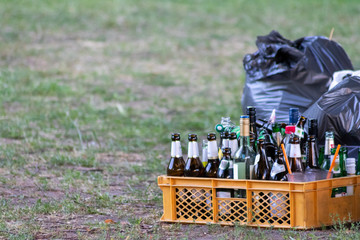 Leere Bierflaschen und leere Weinflaschen stehen nach einer Party neben einem grauen Müllsack als...