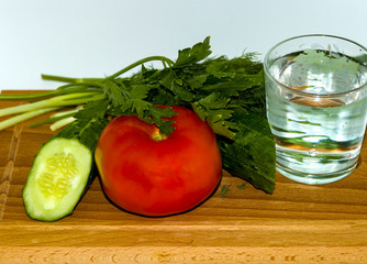 Fresh juicy tomato, green onion, glass of water, sliced cucumber, dill, salad, on wooden chopping Board on white background