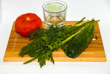 Fresh juicy tomato, green onion, glass of water, sliced cucumber, dill, salad, on wooden chopping Board on white background