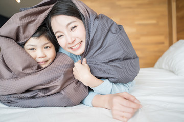 Mother and her daughter child girl playing in the bedroom and putting blanket on . Happy Asian family