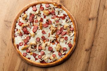 Tasty Italian pizza on wooden  background. Top view of pizza with sausages, chicken, mushrooms, tomatoes and cheese. 