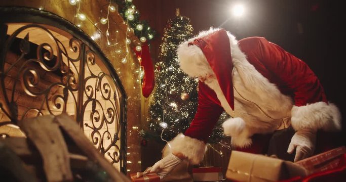 Authentic santa clause leaving christmas gifts near fireplace and christmas tree - chritmas spirit, traditions, holidays and celebrations concept 4k footage