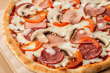 Top view of delicious Capricciosa Pizza on wooden table. Ingredients peeled tomato, cheese, ham, mushrooms, salami.
